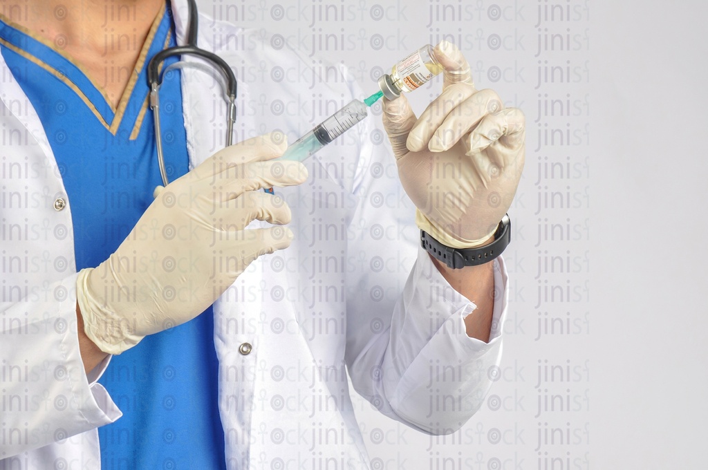 A close-up shot of the hands of a doctor or physician wearing a white coat and preparing a syringe or an injection