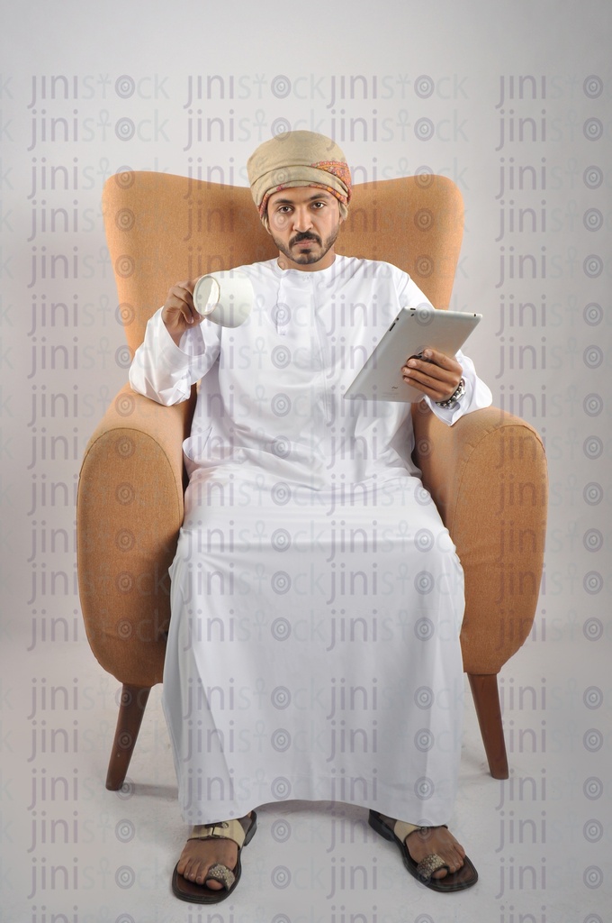 An Omani man from the Gulf wearing an Omani uniform has finished his coffee while sitting on a chair