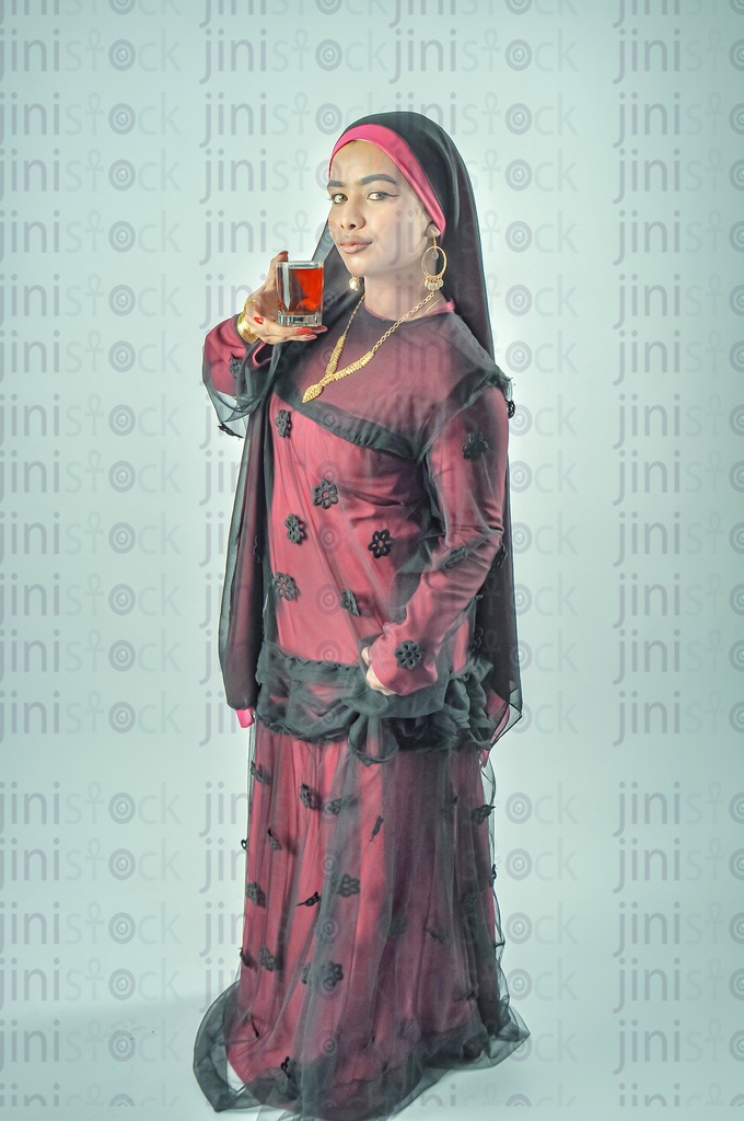 An Egyptian farmer or a Nubian Egyptian woman wearing a Nubian dress, a veil on her head, drinking a cup of tea