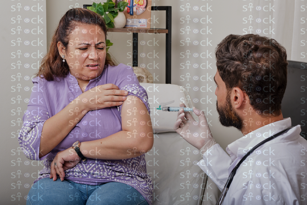 The patient holds her arm in pain while receiving the injection 