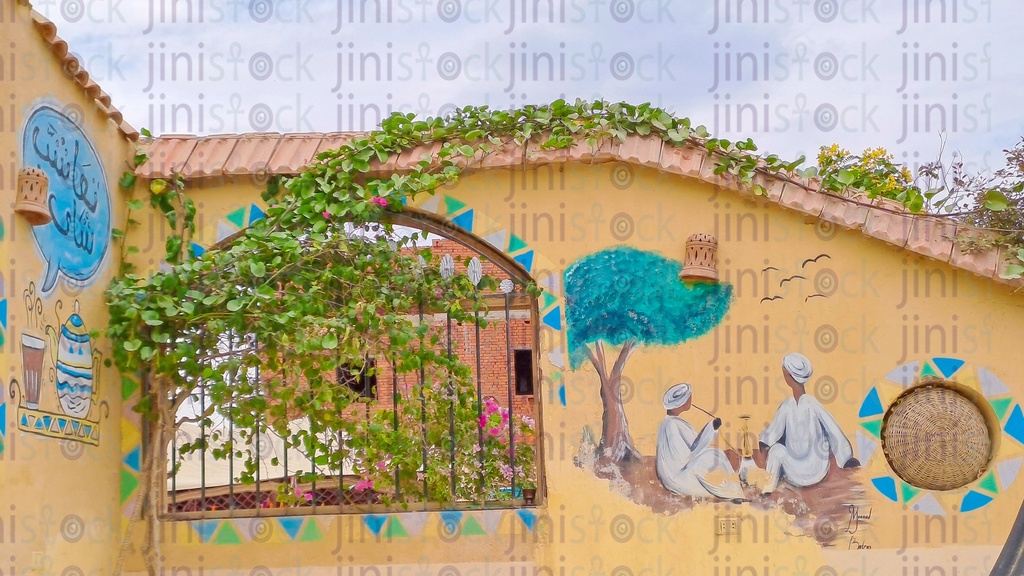 A wall with drawings of two men from Upper Egypt sitting on the ground under a tree, and another drawing of a teapot and a cup of tea.