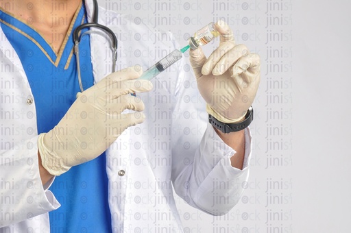 A close-up shot of the hands of a doctor or physician wearing a white coat and preparing a syringe or an injection