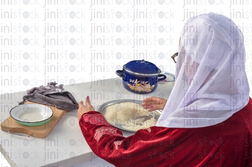 over shoulder shot of an Egyptian woman sitting on a chair and checking the rice on the table before cooking it