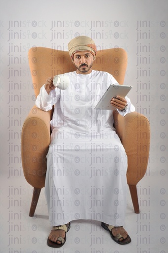 An Omani man from the Gulf wearing an Omani uniform has finished his coffee while sitting on a chair