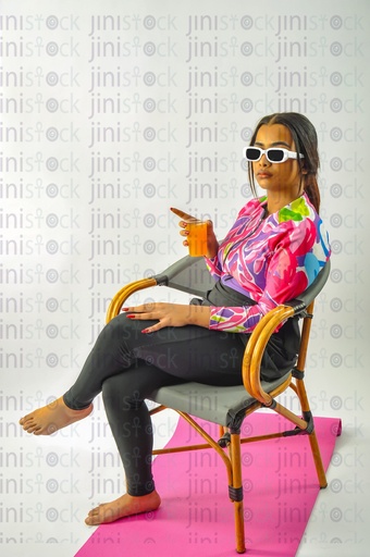 A girl wearing a burkini swimsuit sitting on a chair and drinking orange juice