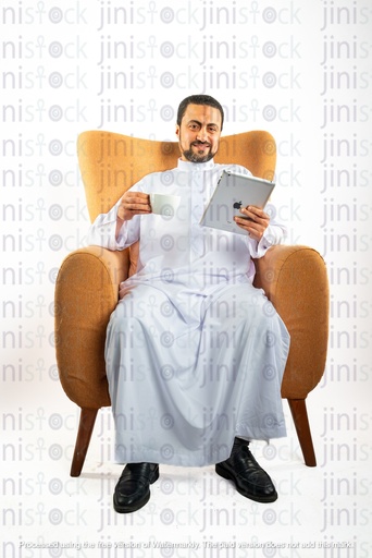 saudi khaliji man sitting on the chair checking his ipad and drinking tea