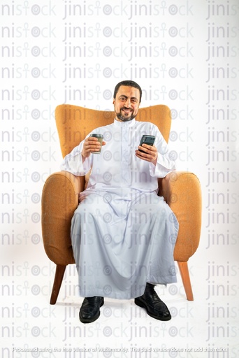 happy saudi khaliji arab man from gulf sitting on a chair holding coffee cup and mobile