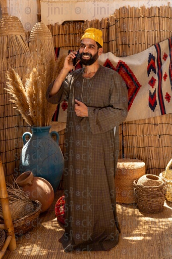 فلاح مصري يقف سعيد يتحدث في الهاتف يرتدي جلباب في كوخ خوص