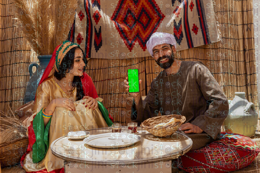  شاب يجلس ممسك هاتف بشاشه خضراء وبجانبة شابه